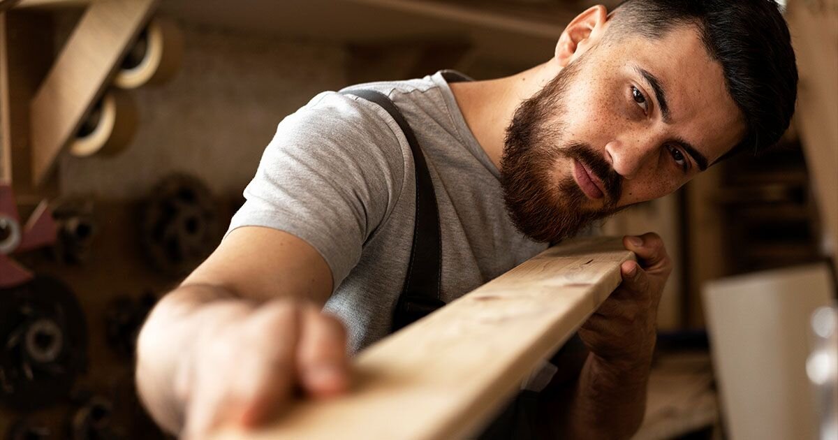 Man holding piece of wood and looking down the plank